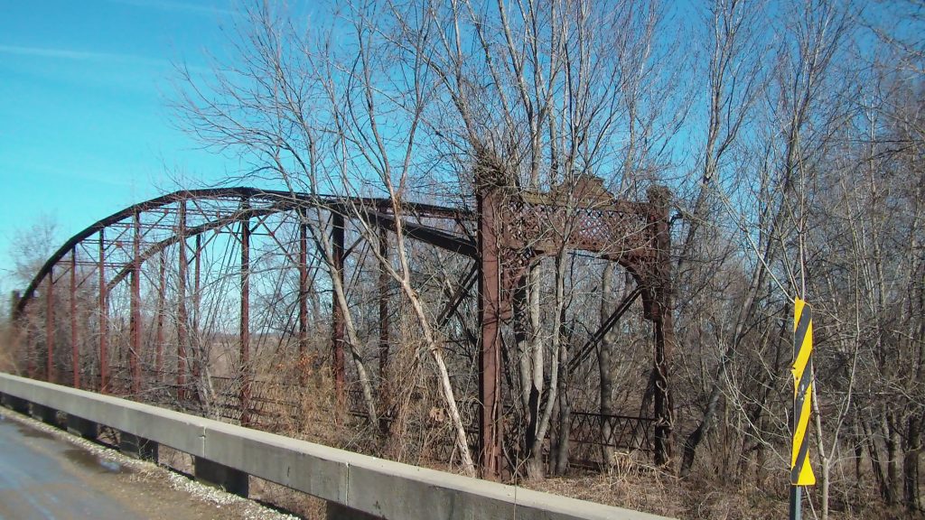 A rusting Pratt truss bridge under a blue winter sky