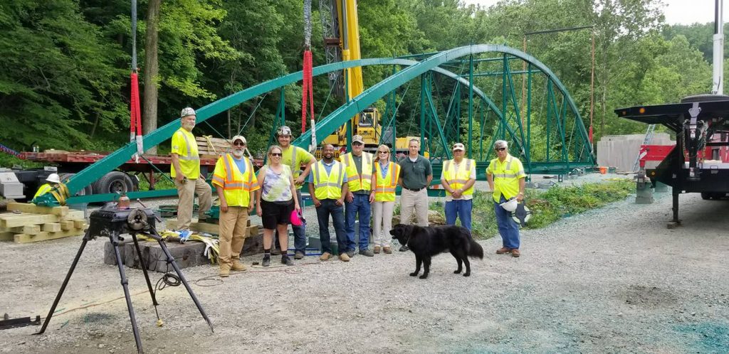 The Workin’ Bridges crew in hard hats in front of a restored green bowstring truss
